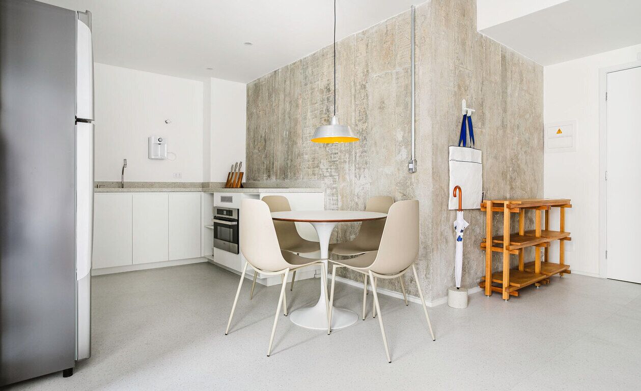 Una cocina moderna con armarios blancos, un refrigerador de acero inoxidable, una mesa redonda con dos sillas y una lámpara colgante.