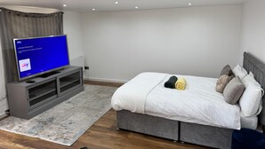 A modern bedroom with a bed, a TV on a stand, and a grey sofa. - Cozy Studio - Near Stadium - Free Parking (Isleworth)
