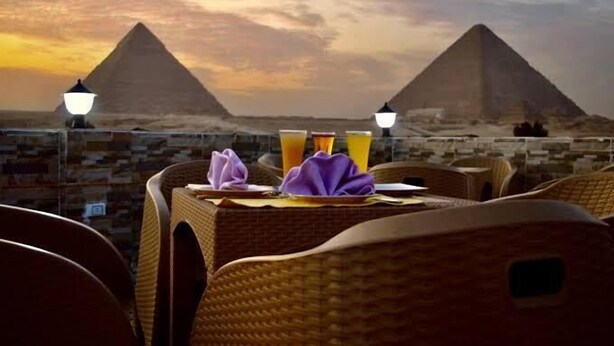 A dining table with a view of the pyramids, two lamps, and a folded purple napkin. - Pharaonic Pyramids Hotel  (Giza)