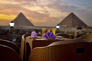 A dining table with a view of the pyramids, two lamps, and a folded purple napkin. - Pharaonic Pyramids Hotel  (Giza)