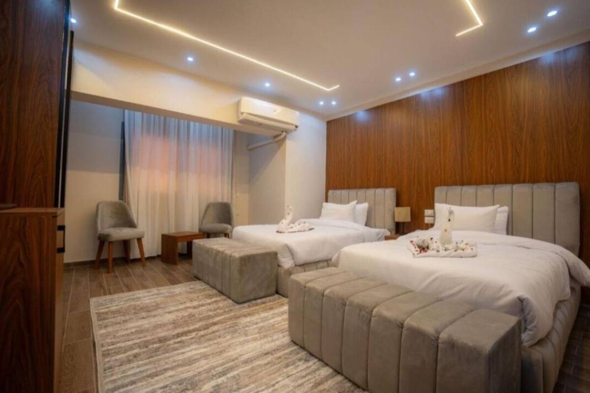 Una habitación de hotel con dos camas, una zona de estar y una pared de madera.