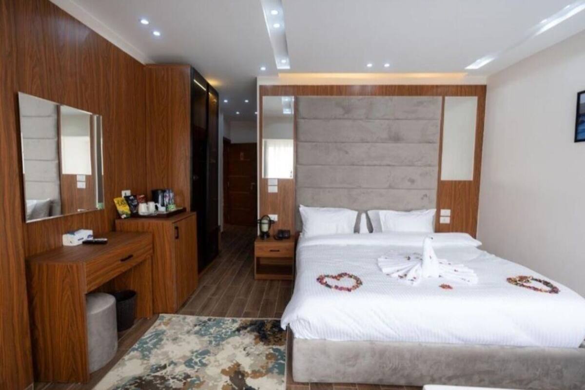 Una habitación de hotel moderna con una cama grande, un armario de madera, mesitas de noche y un espejo.