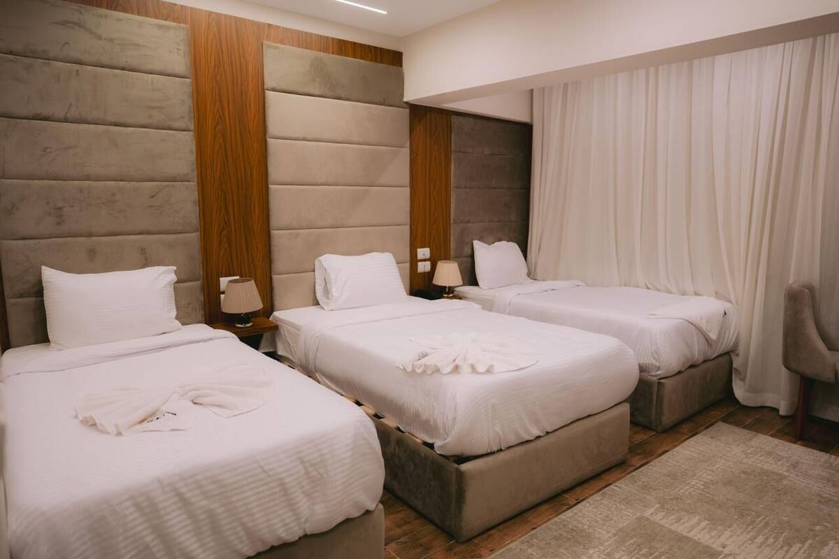 Habitación de hotel con tres camas, paneles de madera en las paredes y un gran ventanal con cortinas.