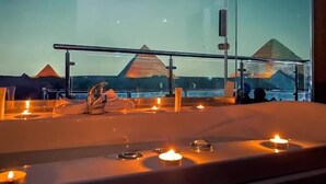 A room with a view of the pyramids, a bathtub with candles, and a glass partition. - Pharaonic Pyramids Hotel  (Giza)