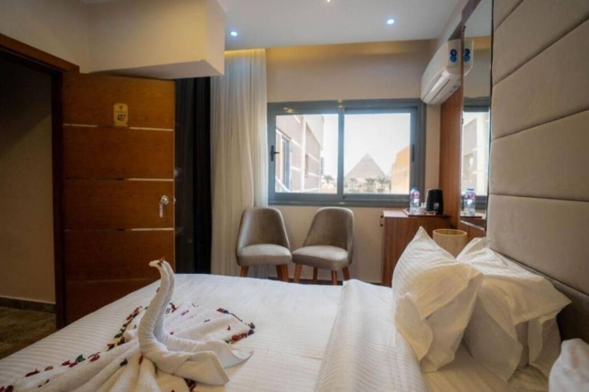 Habitación de hotel con cama, dos sillas, escritorio y ventana con vistas a edificios.