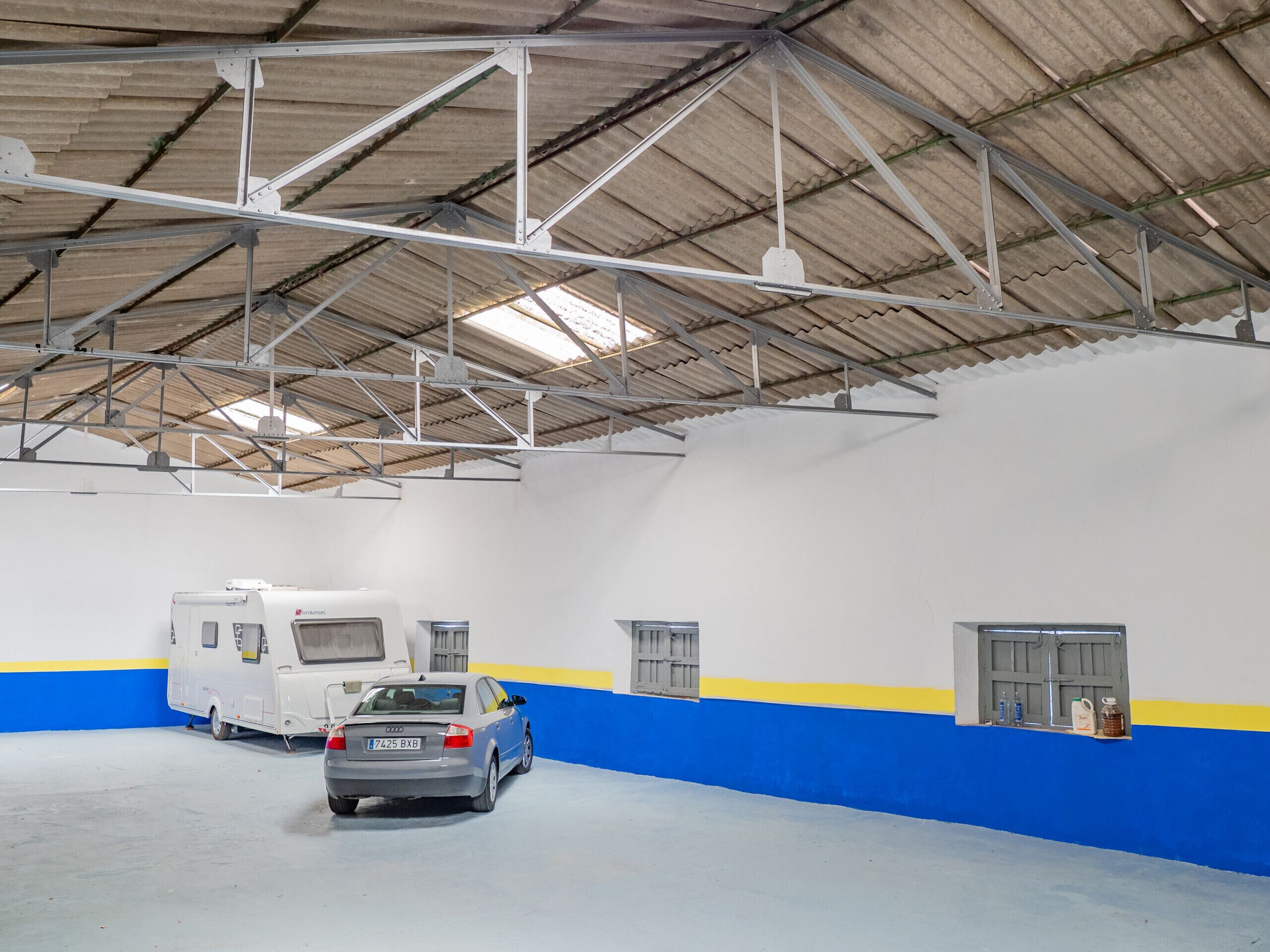 An indoor parking area with a white and blue wall, a silver car, and a white RV.