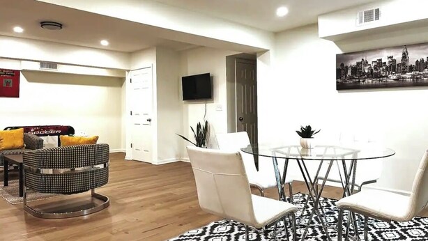 Una sala moderna con una mesa de comedor de vidrio, sillas blancas y una pintura de un paisaje urbano en blanco y negro.