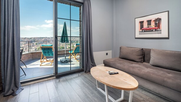 Una sala de estar moderna con un sofá gris, una mesa de centro de madera y un balcón con dos sillas y un parasol verde.
