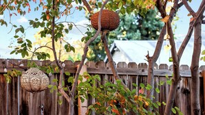 Une clôture en bois d’aspect rustique, une mangeoire à oiseaux suspendue et un panier tressé accroché à une branche d’arbre.