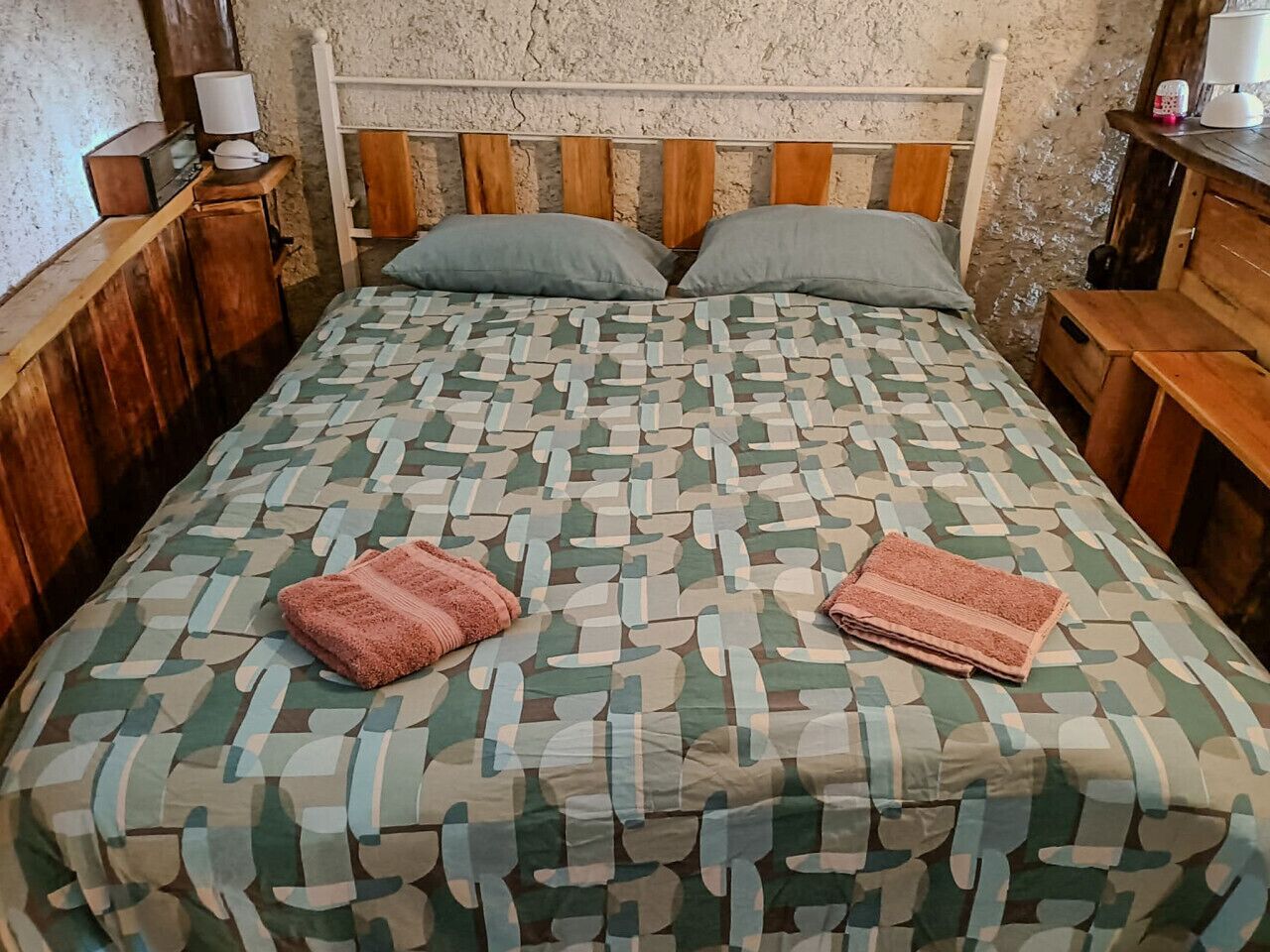 A bed with a patterned bedspread, two pillows, and two folded towels on it.