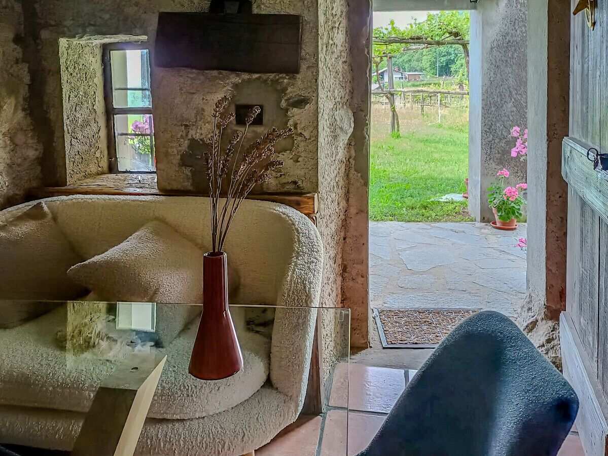 Una habitación rústica con pared de piedra, una mesa de vidrio con un florero y vistas a un jardín por una ventana.