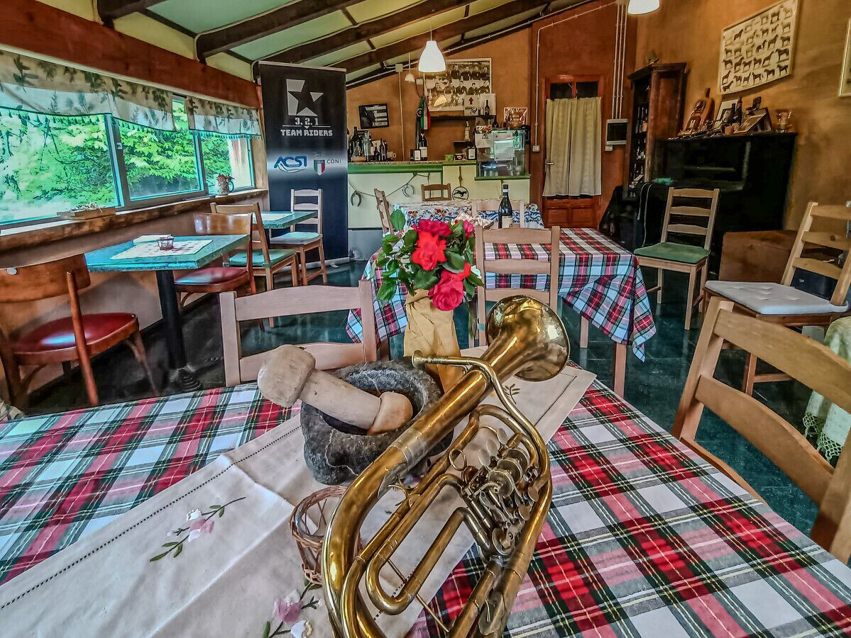 Un interno rustico di ristorante con arredi in legno, tovaglie a quadri e un trombone di ottone su un tavolo.