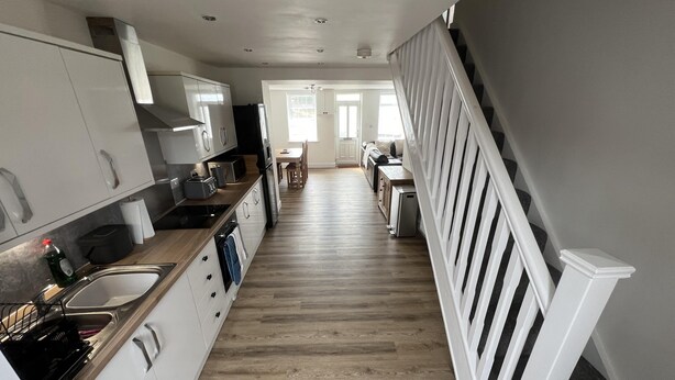 Una cocina moderna con armarios blancos, encimera de madera y una escalera con barandillas blancas que conduce a un comedor.