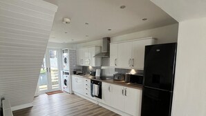 Una cocina moderna con armarios blancos, un refrigerador negro y una mesa de comedor de madera.