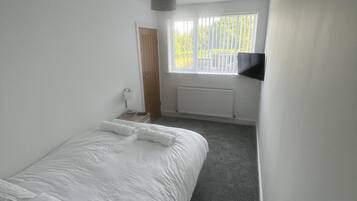 A bedroom with a bed, a radiator, a window with blinds, and a door.