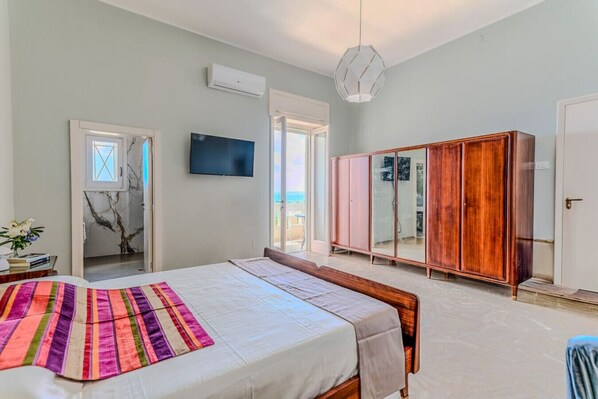 Ein Schlafzimmer mit Bett, Kleiderschrank, Fernseher und Blick ins Freie.