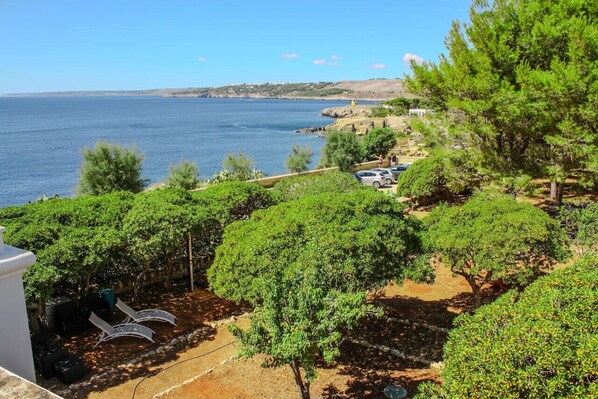 A coastal property with a view of the sea, a paved area with trees, and a parked car.