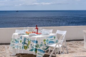Ein Tisch für zwei Personen mit Meerblick, weiße Stühle und eine Tischdecke mit Fischmuster.