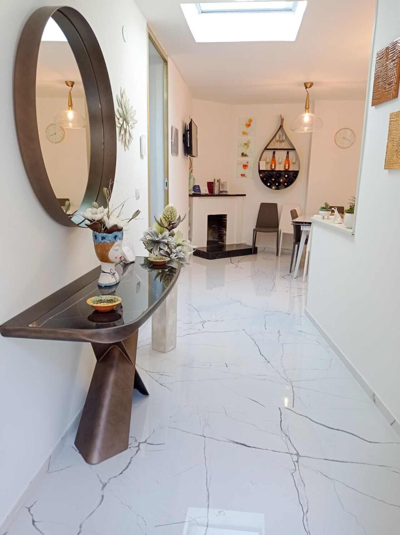 A modern hallway with a marble floor, a large mirror, and a glass-top console table with decorative plants.