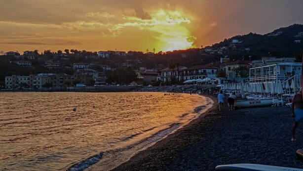 Una playa con un atardecer, edificios al fondo y un bote en la orilla.