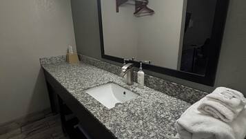 A bathroom with a granite countertop, a white sink, a mirror, and a towel stack.