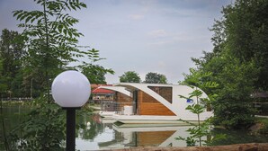 A modern boat with a white exterior and wooden accents, docked near a body of water surrounded by greenery. - Floating Dream, Houseboat (Fiano)