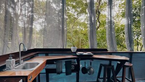 A compact kitchen with a sink, a small stove, and a window overlooking a forest. - Morpho - adventurous Treehouse with amazing 360 view with pool and wifi access (Limón)