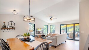 A modern dining area with a wooden table and chairs, a ceiling fan, and a view of the outdoor patio through large windows. - Captain's Quarters, Stylish Lakefront Home, private dock with two slips, 3 bedrooms and 3 bathrooms (Lake Ozark)