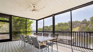 A covered outdoor deck with a table and chairs, overlooking a body of water and greenery. - Captain's Quarters, Stylish Lakefront Home, private dock with two slips, 3 bedrooms and 3 bathrooms (Lake Ozark)