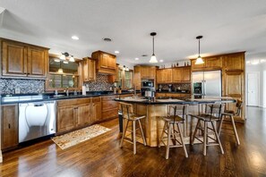 A spacious kitchen with wooden cabinets, a central island with bar stools, and built-in appliances. - Mountain View 4BR Home with Fireplace & Ping Pong (Franklin)