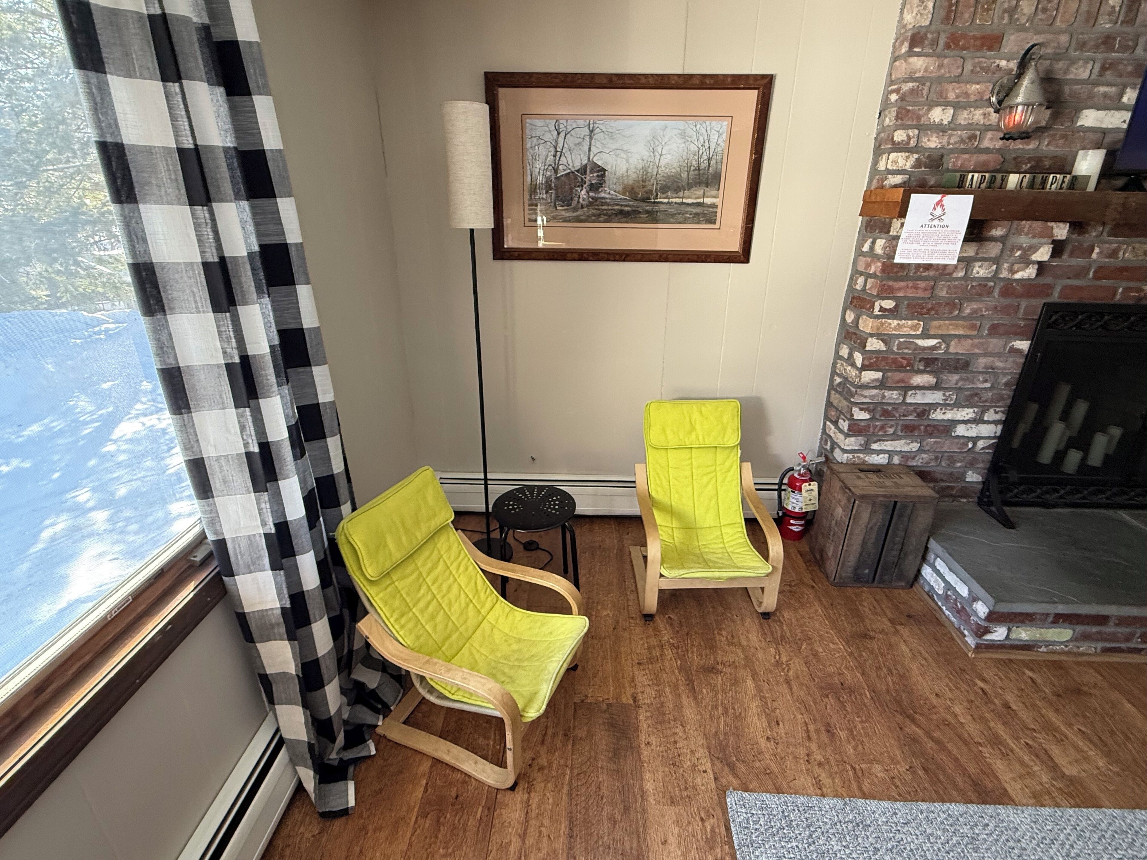 A cozy room with two wooden chairs, a framed picture on the wall, and a brick fireplace.