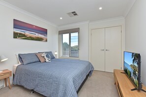 A bedroom with a bed, a window, a door, a TV, and a painting on the wall.