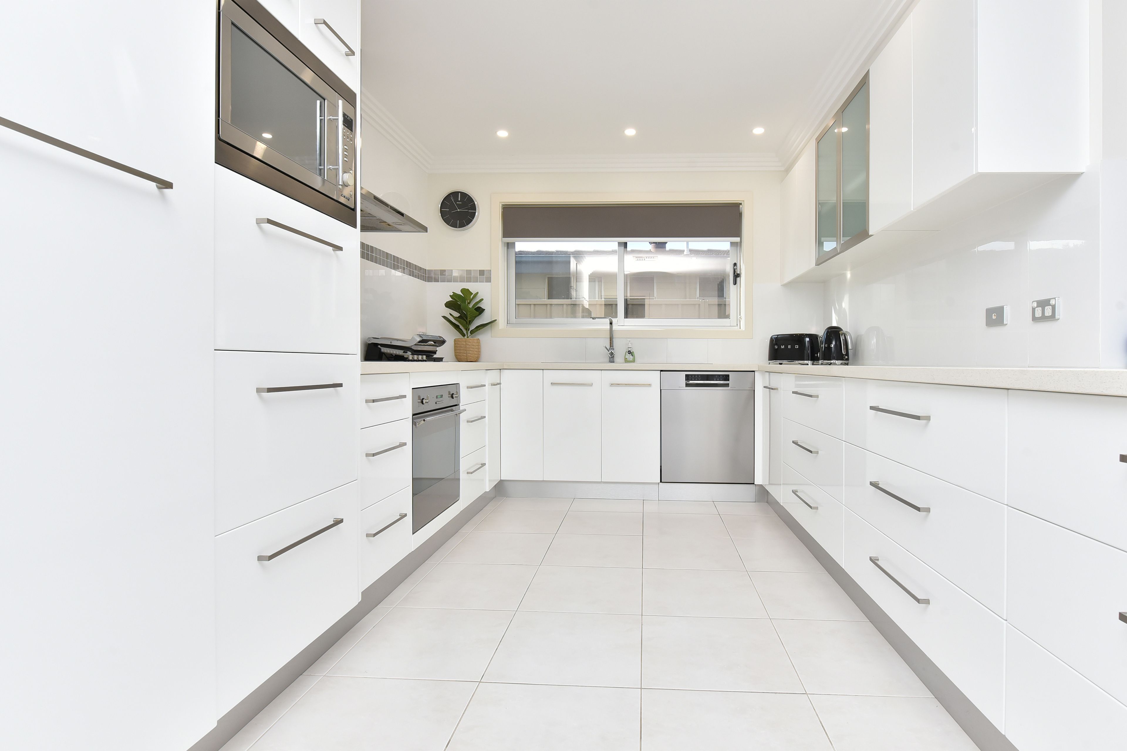 A modern kitchen with white cabinetry, stainless steel appliances, and a large window.