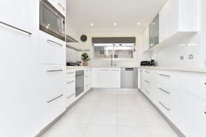 A modern kitchen with white cabinetry, stainless steel appliances, and a large window. - Fingal Bay Retreat close to Beach (Fingal Bay)