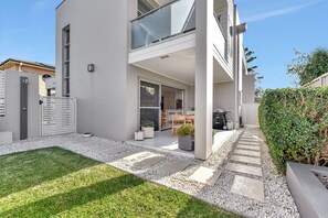 A modern two-story house with a covered patio, a small garden, and a pathway leading to the entrance.
