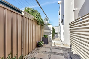 A narrow pathway with stepping stones, flanked by a beige fence and a white building with a garage door. - Fingal Bay Retreat close to Beach (Fingal Bay)