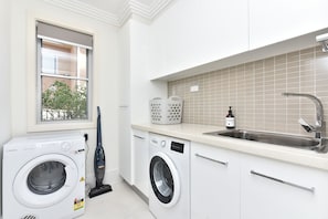 A laundry area with a washing machine, a vacuum cleaner, and a sink with a bottle of soap. - Fingal Bay Retreat close to Beach (Fingal Bay)