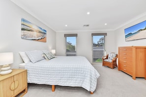 Quarto com cama, cômoda, cadeira e duas janelas.