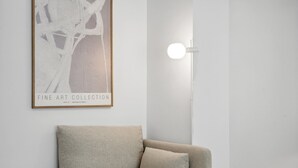 Une pièce au décor minimaliste, avec un canapé beige, une œuvre d’art abstraite encadrée et un luminaire fixé au mur.
