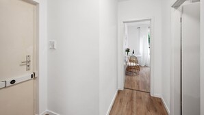 Un couloir aux murs blancs et au plancher en bois mène à une salle à manger équipée d’une table et de chaises.