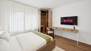 Une chambre à coucher moderne avec un lit, un téléviseur fixé au mur et une armoire en bois.