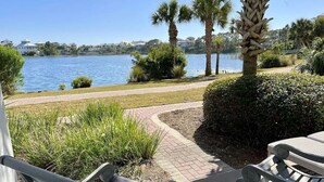 A patio with outdoor seating, a pathway leading to a lake, and palm trees. - Posto Felice! Carillon Beach (Panama City Beach)