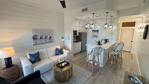 A modern living room with a sofa, coffee table, and dining area with chairs. - Posto Felice! Carillon Beach (Panama City Beach)