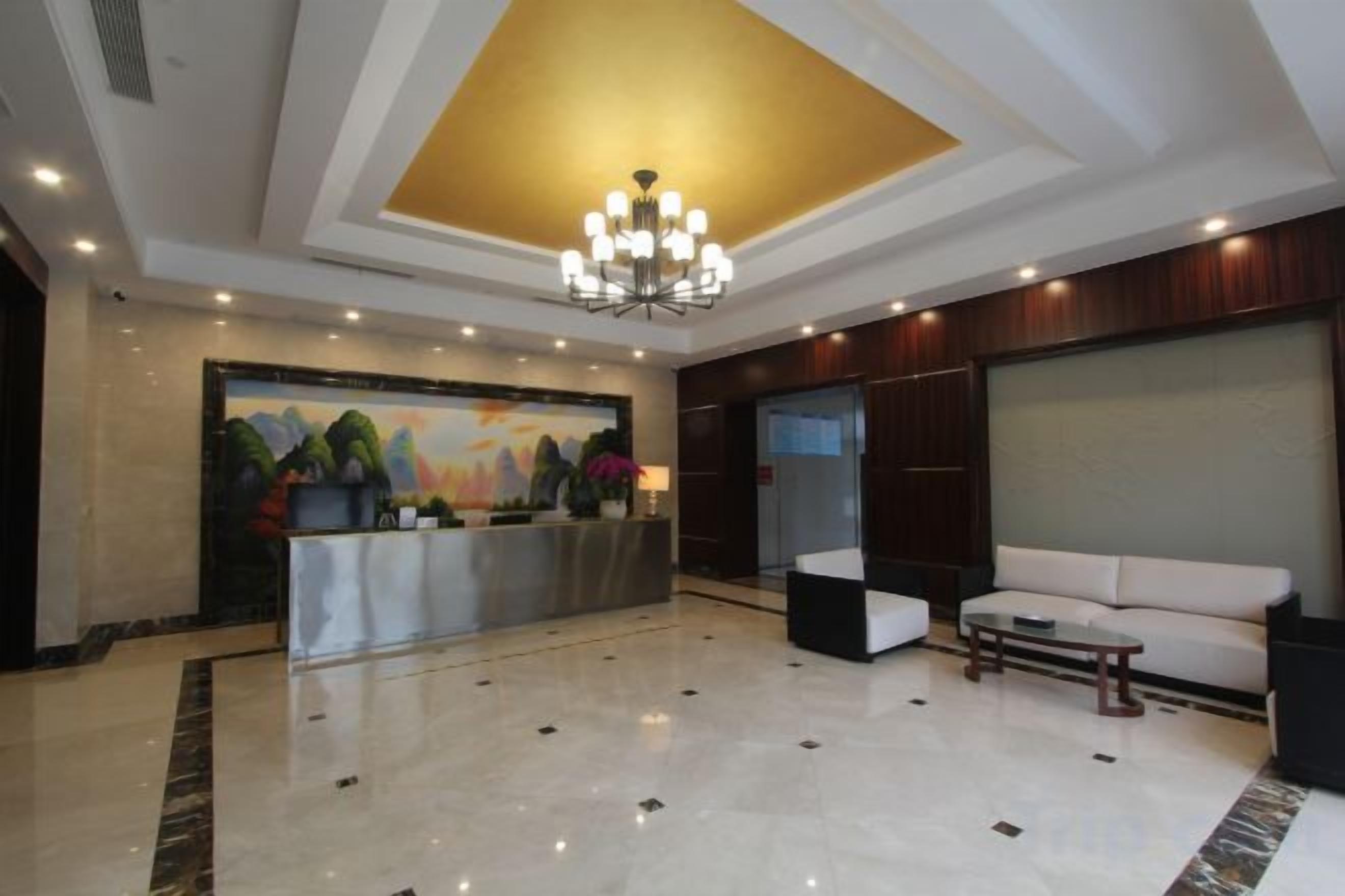 A hotel lobby with a reception desk, a chandelier, a sofa, and a large painting on the wall.