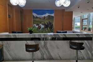 Zona de recepción con mostrador de mármol, dos taburetes de bar, una pintura de caballos y una planta en maceta.