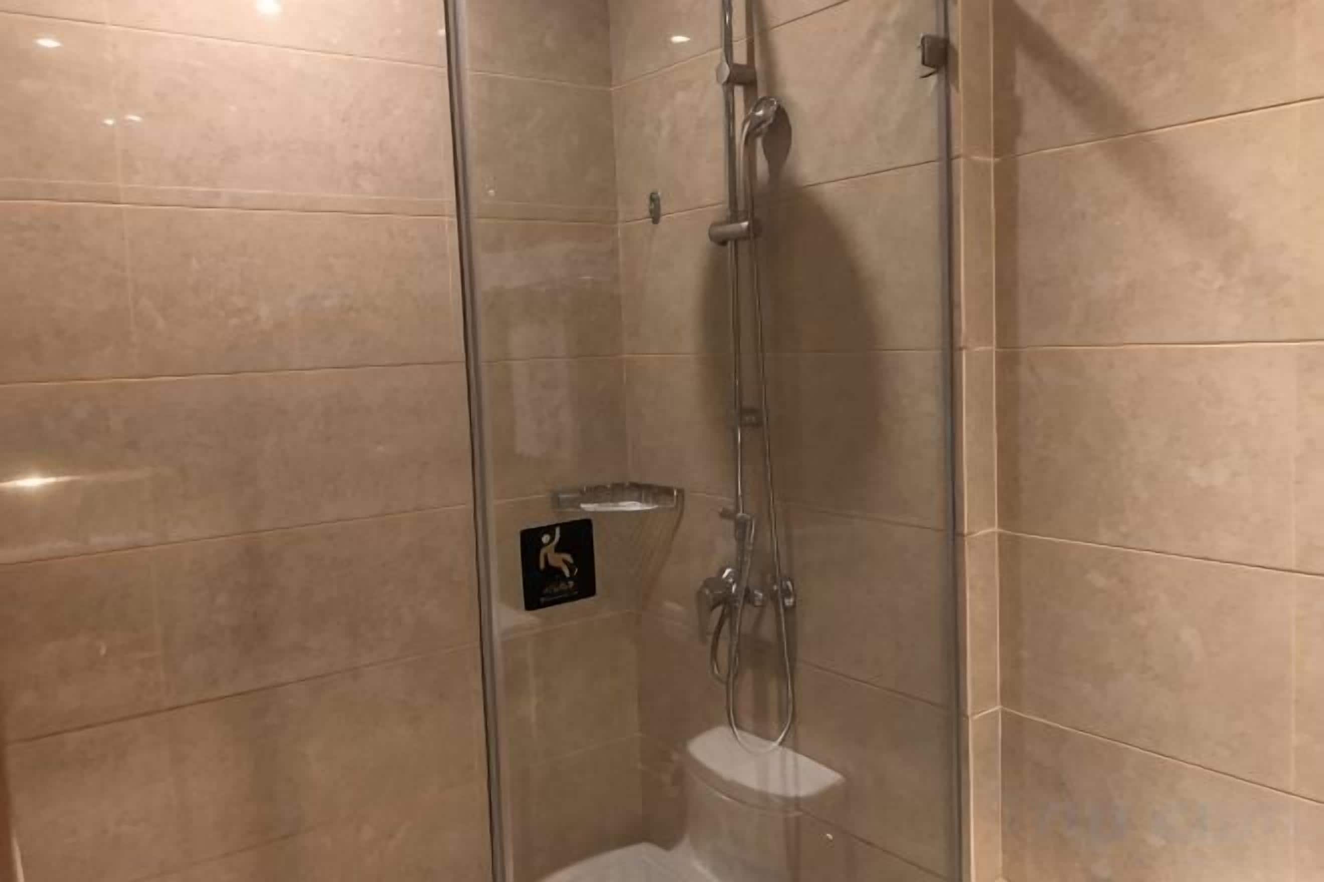 A glass-enclosed shower stall with a handheld showerhead and a wall-mounted faucet.