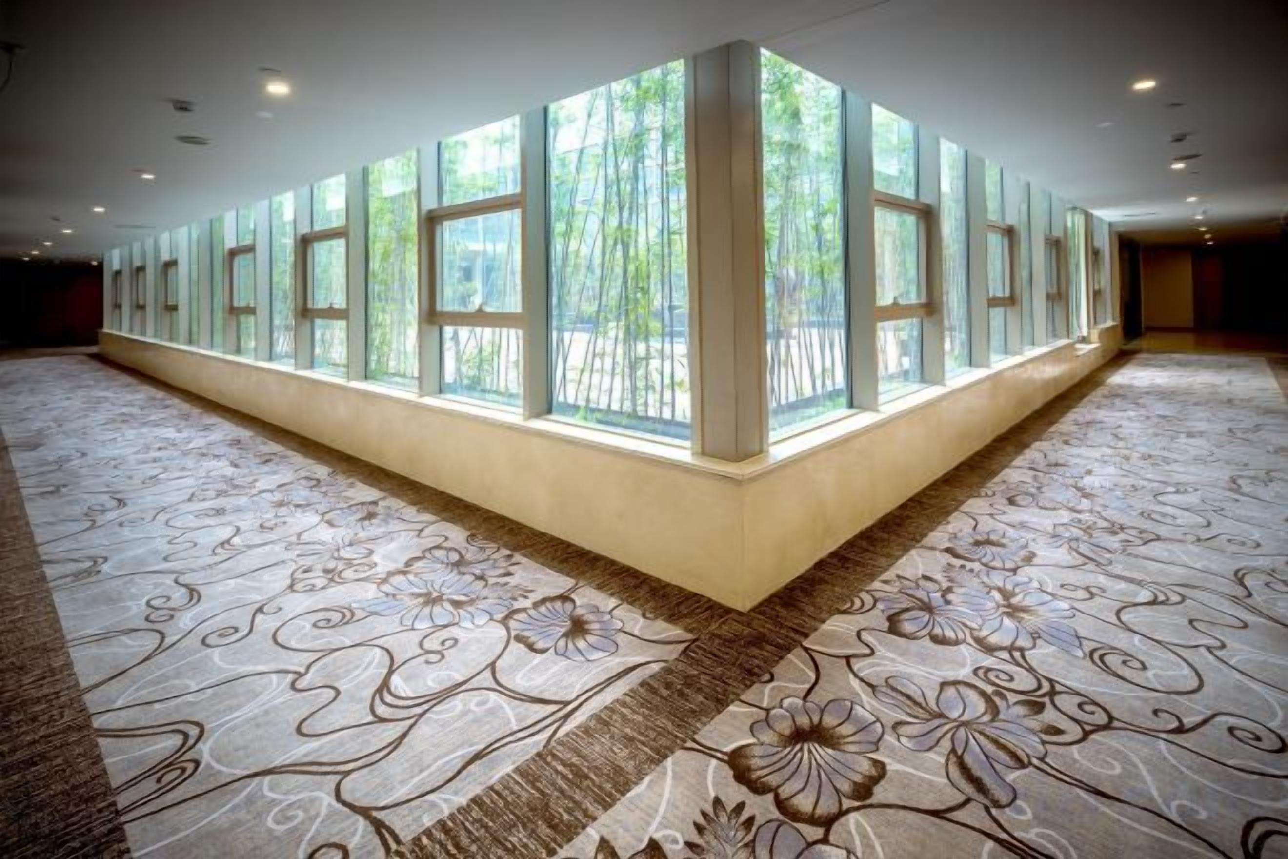 A spacious hallway with patterned carpet, large windows, and a high ceiling.