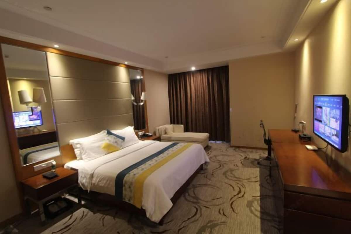 Una camera d'albergo con un letto grande, una scrivania, una sedia, una TV e uno specchio.