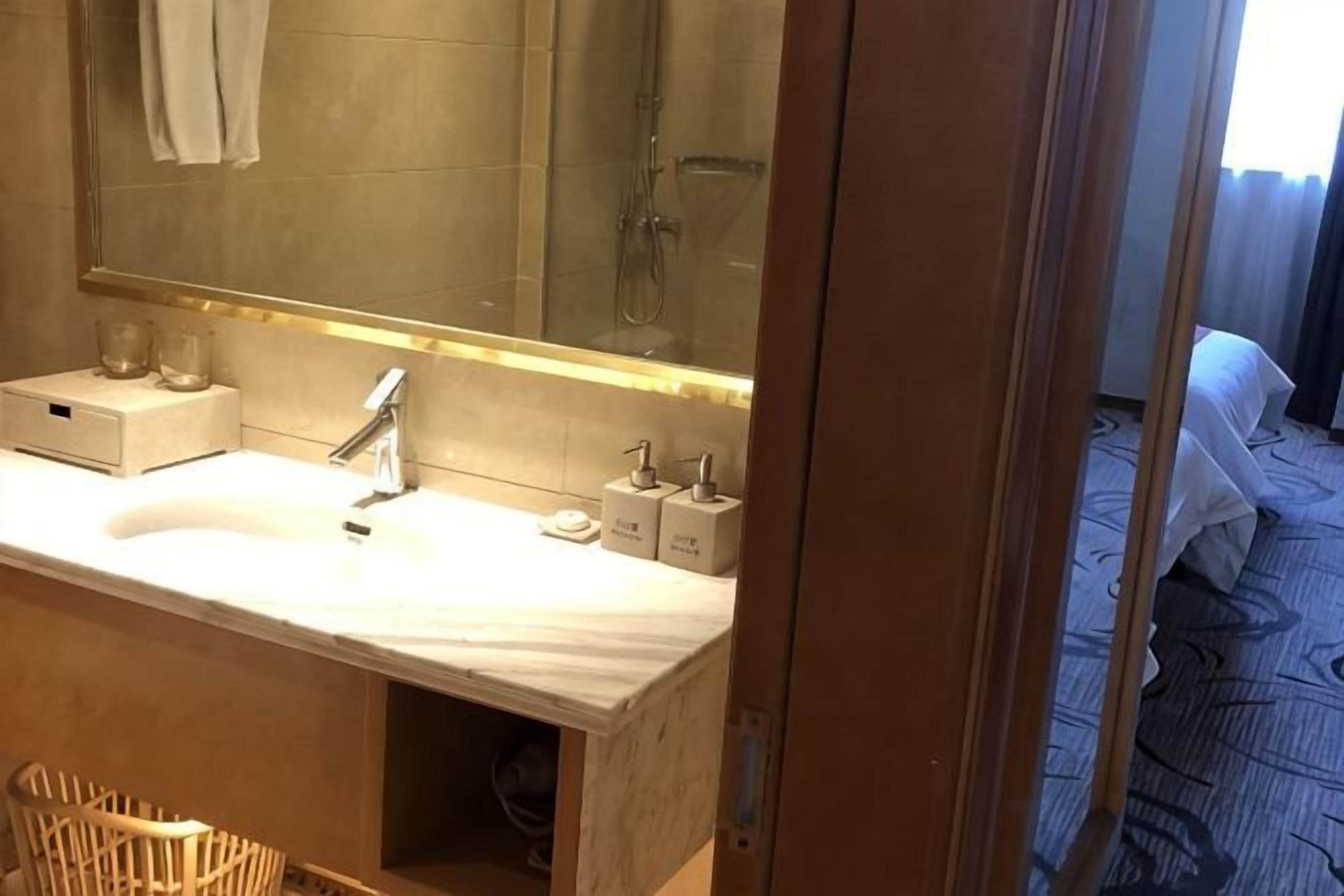 A hotel bathroom with a sink, mirror, and a shower area.