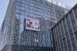 Un bâtiment à la façade quadrillée, une grande enseigne publicitaire et un panneau avec des caractères chinois.